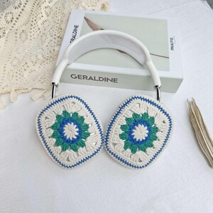 May include: White headphones with crocheted ear covers. The ear covers are white with a blue and green floral pattern.