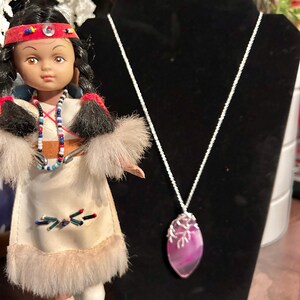 Könnte beinhalten: Eine silberne Kettenkette mit einem Anhänger aus rosa und weißem Achat. Der Anhänger ist tropfenförmig und hat einen silbernen Draht um den Rand. Die Kette wird auf einem schwarzen Samtständer präsentiert.