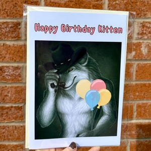 May include: Birthday card with a cartoon wolf wearing a cowboy hat, holding balloons. The card has the text "Happy Birthday Kitten" in pink letters. The wolf is gray and white with yellow eyes.