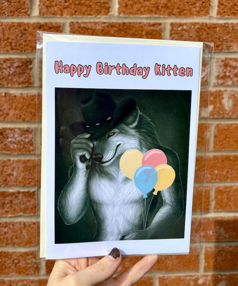 May include: Birthday card with a cartoon wolf wearing a cowboy hat, holding balloons. The card has the text "Happy Birthday Kitten" in pink letters. The wolf is gray and white with yellow eyes.