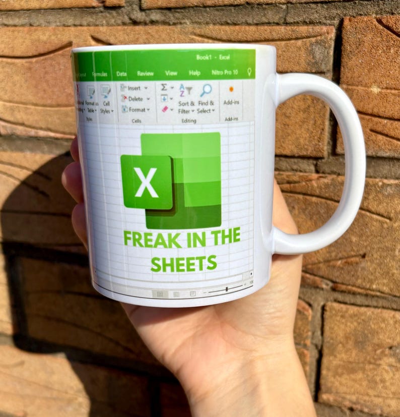 K&ouml;nnte beinhalten: Eine wei&szlig;e Kaffeetasse mit einem gr&uuml;nen Excel-Tabellenblatt-Design. Die Tasse tr&auml;gt den Text "FREAK IN THE SHEETS".