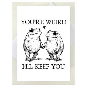 Puede incluir: Una tarjeta de felicitaci&oacute;n blanca con una ilustraci&oacute;n en blanco y negro de dos ranas tomadas de la mano. El texto "YOU'RE WEIRD, I'LL KEEP YOU" est&aacute; impreso encima y debajo de las ranas. Un peque&ntilde;o coraz&oacute;n negro est&aacute; entre las ranas.