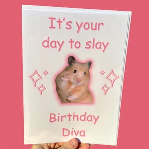 May include: A white card with pink text that reads "It's your day to slay Birthday Diva". A hamster with a pink halo is pictured in the center of the card.