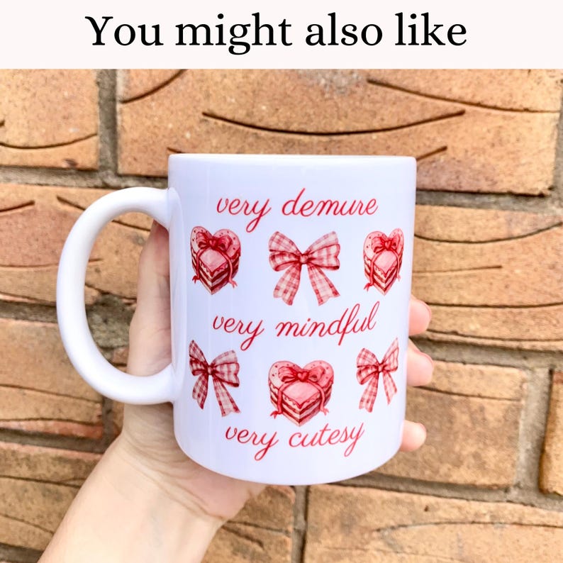May include: White ceramic mug with a pink and red design. The mug has a handle and features the text "very demure", "very mindful", and "very cutesy" with pink and red bows and hearts.