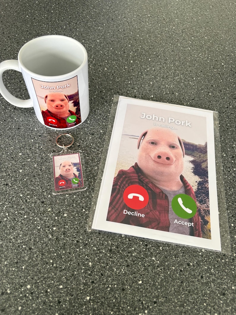 Puede incluir: Una taza blanca con una imagen de un cerdo con un tel&eacute;fono en la pantalla. El texto "John Pork is calling..." est&aacute; en la taza. Hay un llavero a juego con un cerdo y un tel&eacute;fono en la pantalla. Tambi&eacute;n hay una tarjeta con un cerdo con un tel&eacute;fono en la pantalla. El texto "John Pork is calling..." est&aacute; en la tarjeta. Hay dos botones en el tel&eacute;fono, uno rojo con la palabra "Rechazar" y uno verde con la palabra "Aceptar".