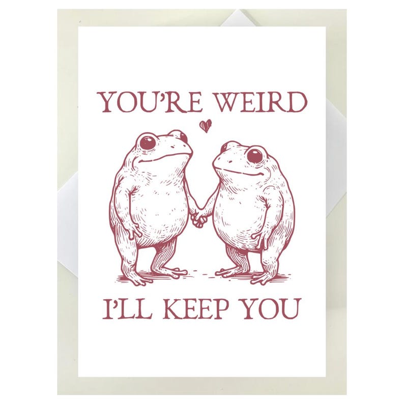 Puede incluir: Una tarjeta de felicitaci&oacute;n blanca con una ilustraci&oacute;n granate de dos ranas tomadas de la mano, con el texto "YOU'RE WEIRD, I'LL KEEP YOU". Un peque&ntilde;o coraz&oacute;n est&aacute; encima de las ranas. La tarjeta est&aacute; dentro de un sobre blanco.