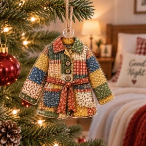 Könnte beinhalten: Ein flacher, transparenter Acryl-Weihnachtsbaumschmuck in Form eines gesteppten Mantels. Der Mantel zeigt ein Patchwork-Design mit verschiedenen Blumen- und Karomustern in Rot, Grün, Gelb und Blau. Er ist mit drei Knöpfen und einem Gürtel versehen.