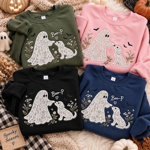 Puede incluir: Cuatro sudaderas de cuello redondo en verde oliva, rosa claro, negro y azul marino. Cada una presenta un diseño bordado de un fantasma y un cachorro con detalles de encaje, flores, murciélagos y el texto "Boo-P" con un pequeño corazón.