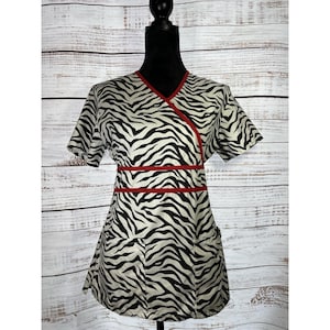 May include: A short-sleeved wrap top with a zebra print in black and white. The top has red trim along the neckline and waist. The garment is displayed on a black mannequin against a light wood-paneled background.