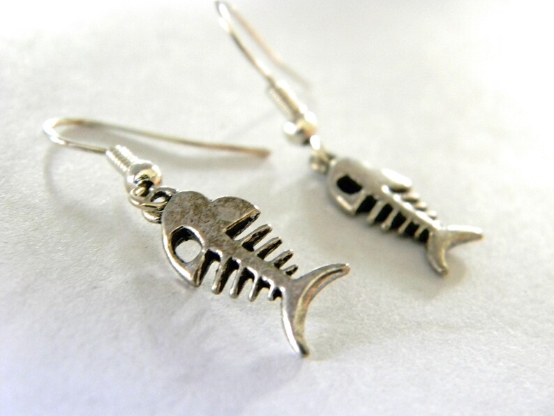 May include: A pair of silver fish bone earrings. The earrings are dangle style and feature a detailed fish bone design.