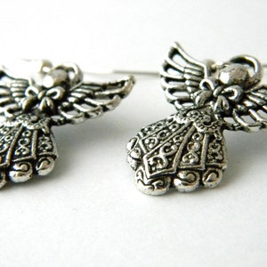 May include: A pair of silver angel earrings with intricate details. The angels have wings and a detailed dress with a bow at the neck.