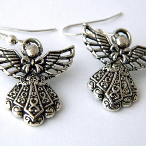 May include: A pair of silver angel dangle earrings. The angels have detailed wings and a bow at the neck. The earrings are on a white background.