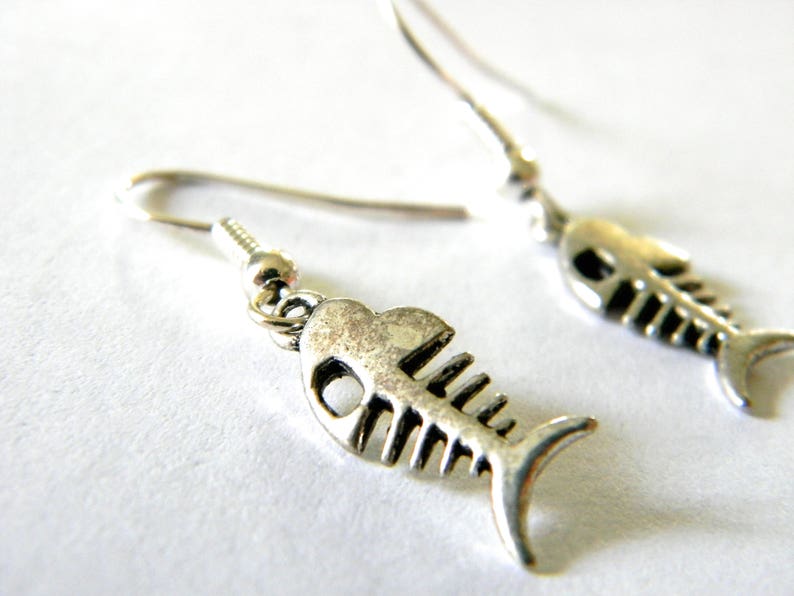 May include: A pair of silver fish bone earrings. The earrings are made of metal and have a detailed fish bone design.