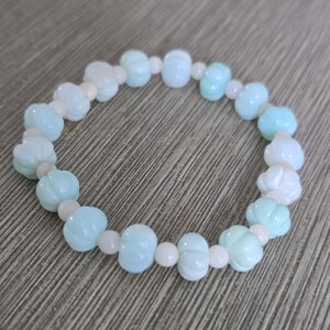 May include: A stretch bracelet featuring alternating light blue, pumpkin-shaped beads and small, round, pale cream-colored spacer beads. The light blue beads have a ribbed, textured surface, while the cream beads are smooth and opaque.