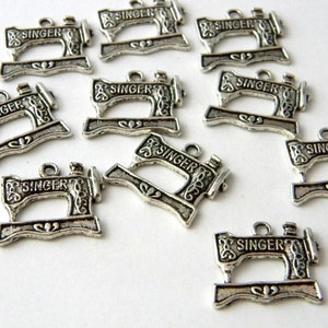 May include: A collection of silver-colored metal charms shaped like vintage Singer sewing machines. Each charm has the word "SINGER" across the top and a small loop for attaching to jewelry or other crafts.