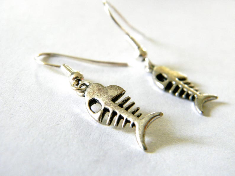 May include: A pair of silver fish bone earrings. The earrings are dangle style and feature a detailed fish bone design.