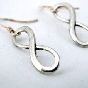 May include: A pair of silver infinity symbol earrings. The earrings are made of a smooth, textured metal and have a simple, elegant design.