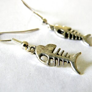 May include: A pair of silver fish bone dangle earrings. The earrings are made of metal and have a detailed fish bone design.