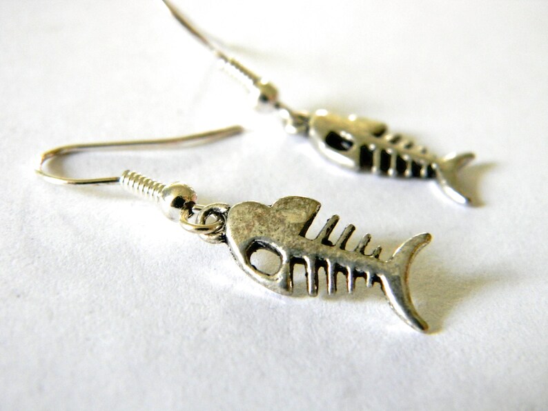 May include: A pair of silver fish bone dangle earrings. The earrings are made of metal and have a detailed fish bone design.