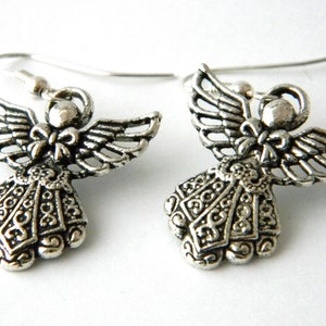 May include: A pair of silver angel earrings with intricate details. The angels have wings, a bow, and a detailed dress.