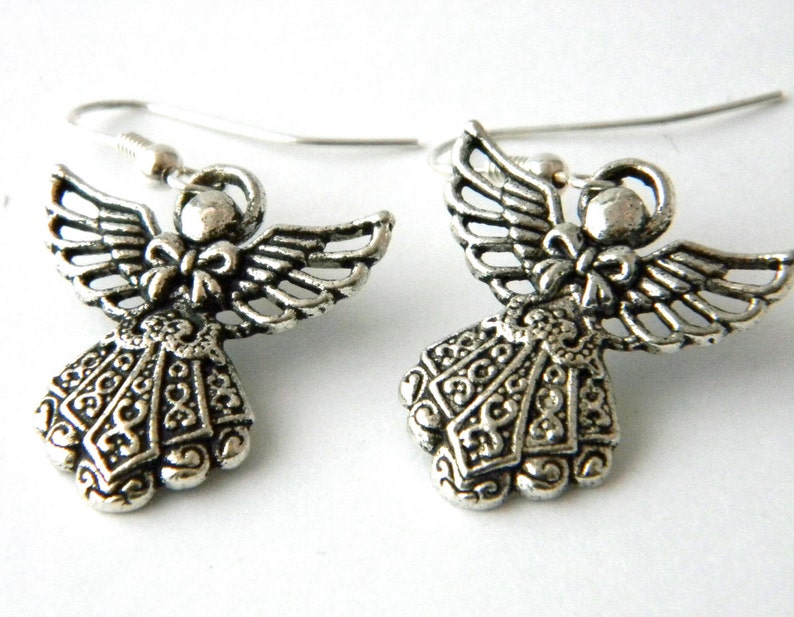 May include: A pair of silver angel earrings with intricate details. The angels have wings, a bow, and a detailed dress.