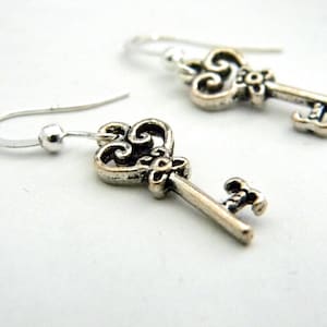 May include: A pair of silver key-shaped earrings with ornate details. The keys have a heart-shaped top and a small flower design.