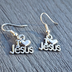 Pu&ograve; includere: Orecchini d'argento con un cuore e le parole "I Love Jesus" appese a un gancio d'argento.