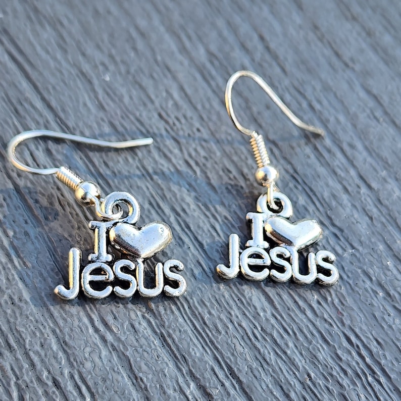 Pu&ograve; includere: Orecchini d'argento con un cuore e le parole "I Love Jesus" appese a un gancio d'argento.