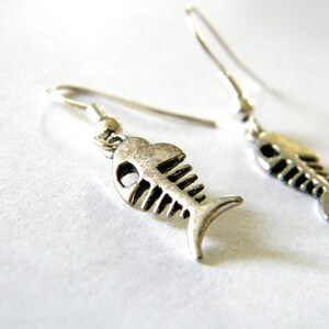 May include: A pair of silver fish bone earrings. The earrings are dangle style and feature a detailed fish bone design.