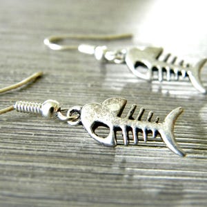 May include: A pair of silver fish bone earrings. The earrings are made of metal and have a detailed fish bone design.