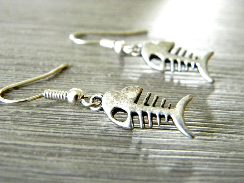 May include: A pair of silver fish bone earrings. The earrings are made of metal and have a detailed fish bone design.