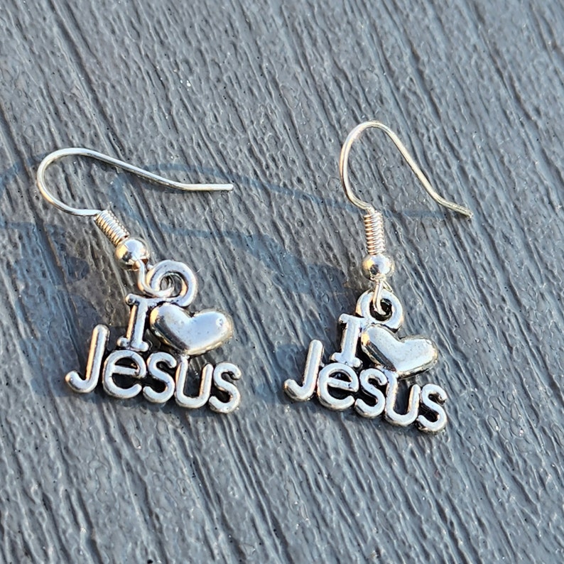 Pu&ograve; includere: Un paio di orecchini d'argento con un cuore e le parole "I love Jesus" che pendono dal fondo.