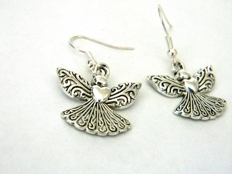 Puede incluir: Pendientes de aro de plata con un dise&ntilde;o de &aacute;ngel detallado con un coraz&oacute;n en el centro. Las alas del &aacute;ngel tienen un patr&oacute;n de espiral.