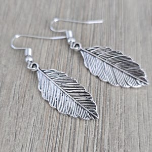 May include: A pair of silver feather earrings with a detailed design. The earrings are dangle style with a hook closure.