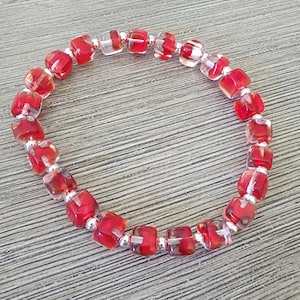 May include: Red and clear glass square beads strung on a silver chain to form a bracelet.