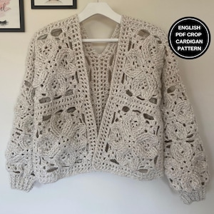Può includere: Un cardigan all'uncinetto con un motivo traforato di colore beige chiaro. Il cardigan ha un collo a V e maniche lunghe. Il testo "ENGLISH PDF CROP CARDIGAN PATTERN" è visibile nell'angolo in alto a destra dell'immagine.