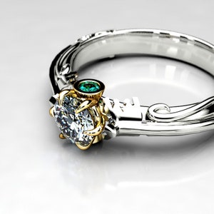 May include: A silver and gold engagement ring with a large, round, clear diamond and a small, round, green gemstone. The ring has a delicate, ornate design.