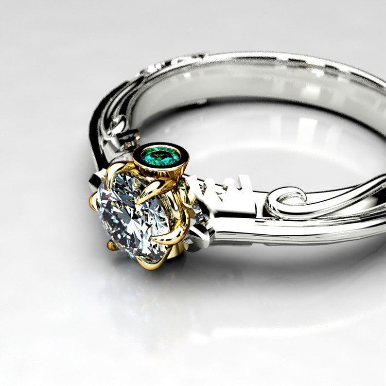 May include: A silver and gold engagement ring with a large, round, clear diamond and a small, round, green gemstone. The ring has a delicate, ornate design.