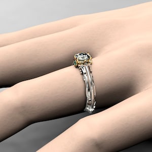 May include: A gold and white engagement ring with a large center diamond and two smaller emerald green stones on the band.