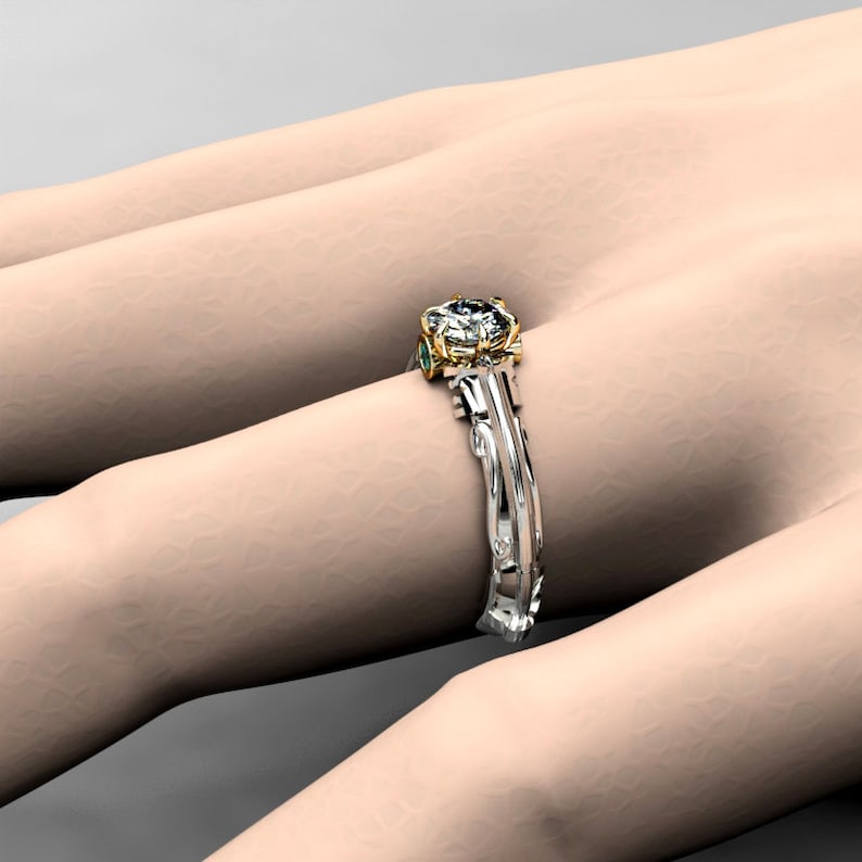 May include: A gold and white engagement ring with a large center diamond and two smaller emerald green stones on the band.
