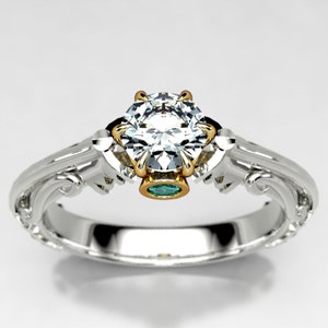 May include: A white gold engagement ring with a large, round, clear diamond center stone. The ring has a delicate, ornate design with a small green emerald stone set in the band.