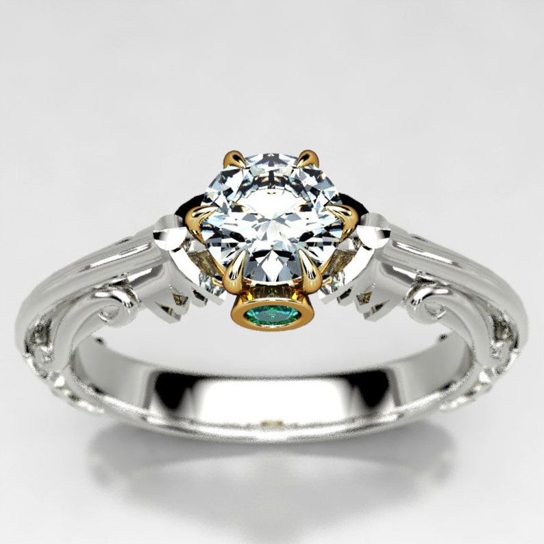 May include: A white gold engagement ring with a large, round, clear diamond center stone. The ring has a delicate, ornate design with a small green emerald stone set in the band.