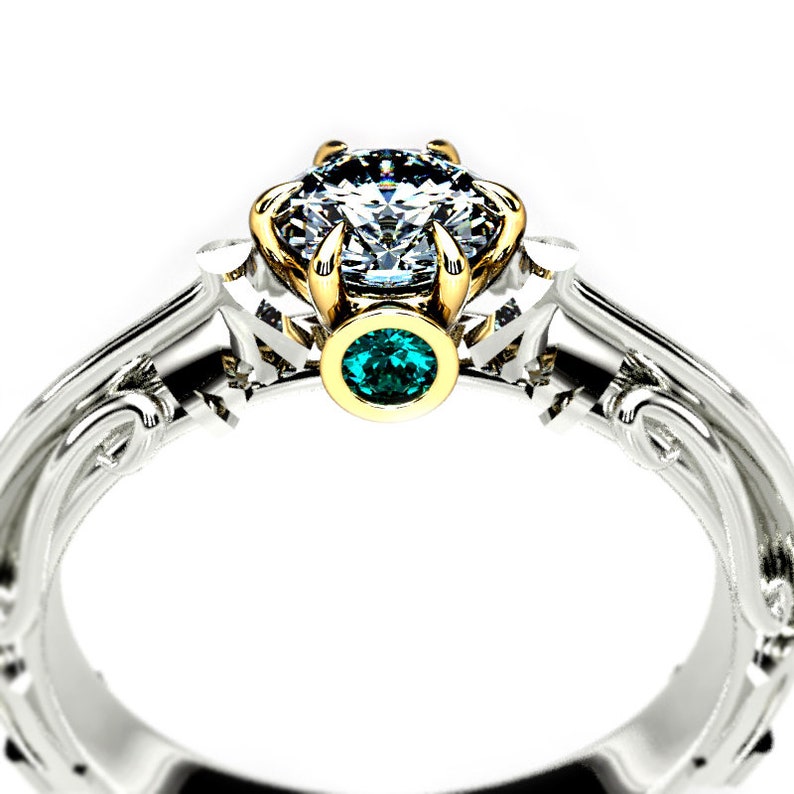 May include: A silver and gold engagement ring with a large, clear diamond center stone and a smaller, emerald green gemstone on the band.