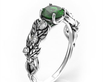 Könnte beinhalten: Ein silberner Ring mit einem grünen Edelstein und kleineren klaren Edelsteinen, die in einem Blattdesign eingefasst sind.