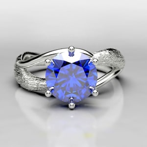 Puede incluir: Un anillo de plata con una banda retorcida y una gran piedra preciosa de zafiro azul redonda.