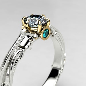 May include: A silver and gold ring with a large, clear diamond and a smaller, teal blue gemstone. The ring has a delicate, floral design.