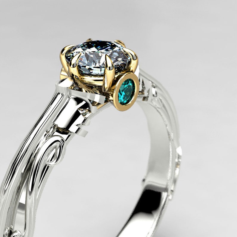 May include: A silver and gold ring with a large, clear diamond and a smaller, teal blue gemstone. The ring has a delicate, floral design.