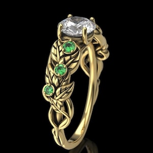 Puede incluir: Un anillo de oro con una piedra central grande y transparente y cuatro piedras verdes más pequeñas engastadas en un diseño de hojas.