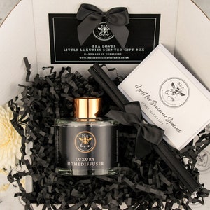 May include: A gift box filled with black shredded paper, a black and gold luxury home diffuser bottle, a black and white card with the text "A gift for someone special, sent with love", and black diffuser sticks.