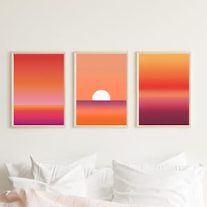 Op de afbeelding: Drie abstracte zonsondergang-verloopdrukken in een set. De prints tonen een verloop van oranje, rood en roze kleuren. De middelste print heeft een witte cirkel in het midden, die de zon voorstelt.